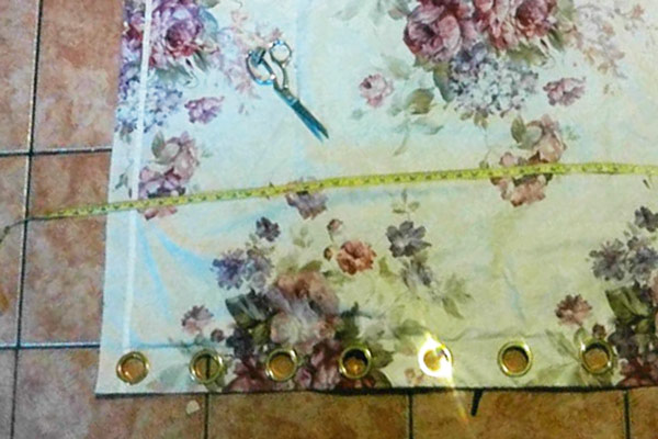 A pink floral curtain with brass eyelets, laid out with a tape measure
