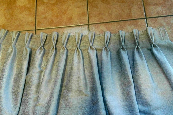Pinch pleats sewn by hand across the top of a blue curtain